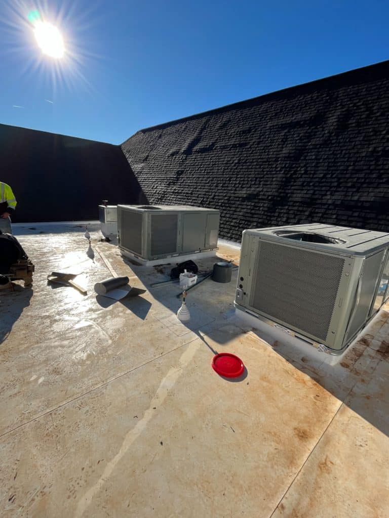 Rooftop with three air conditioning units and a red frisbee on the ground under a clear sky with bright sun.