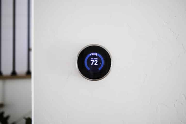 A modern, circular digital thermostat mounted on a white wall displays a temperature of 72 degrees Fahrenheit.