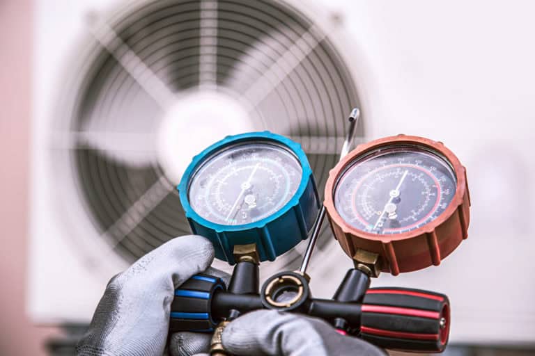 Close-up of gloved hands holding pressure gauges in front of a large industrial fan.