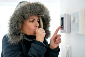 Cold woman pressing thermostat during an emergency heating system repair.