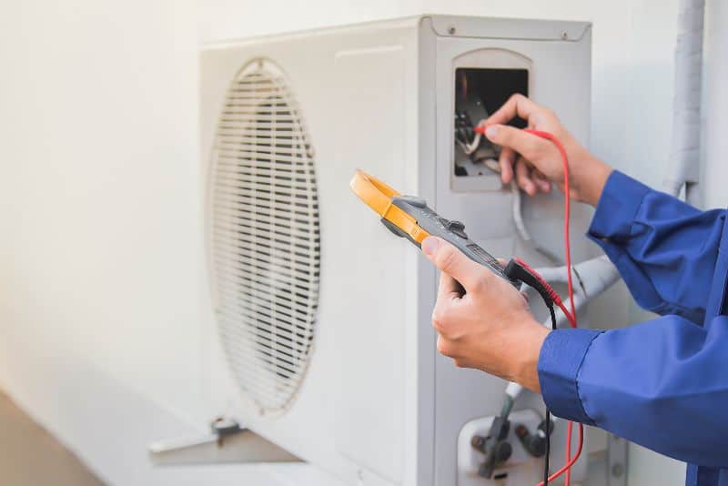 Person using a multimeter to check electrical connections on an outdoor air conditioning unit.