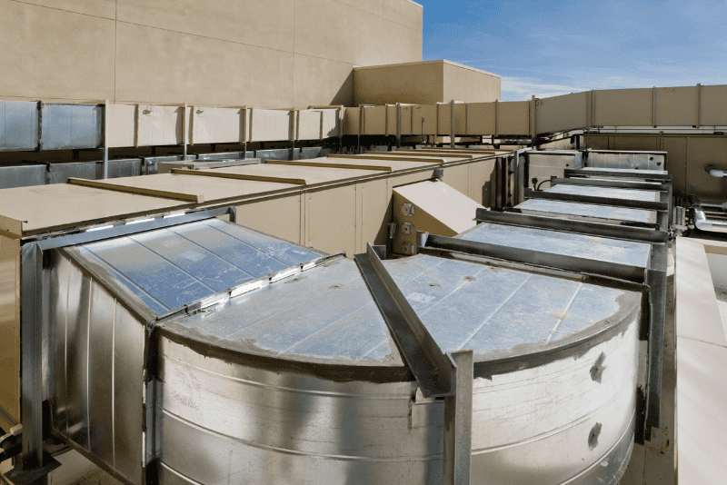 Rooftop HVAC system with large metal ducts and vents attached to a commercial building, under a clear blue sky.