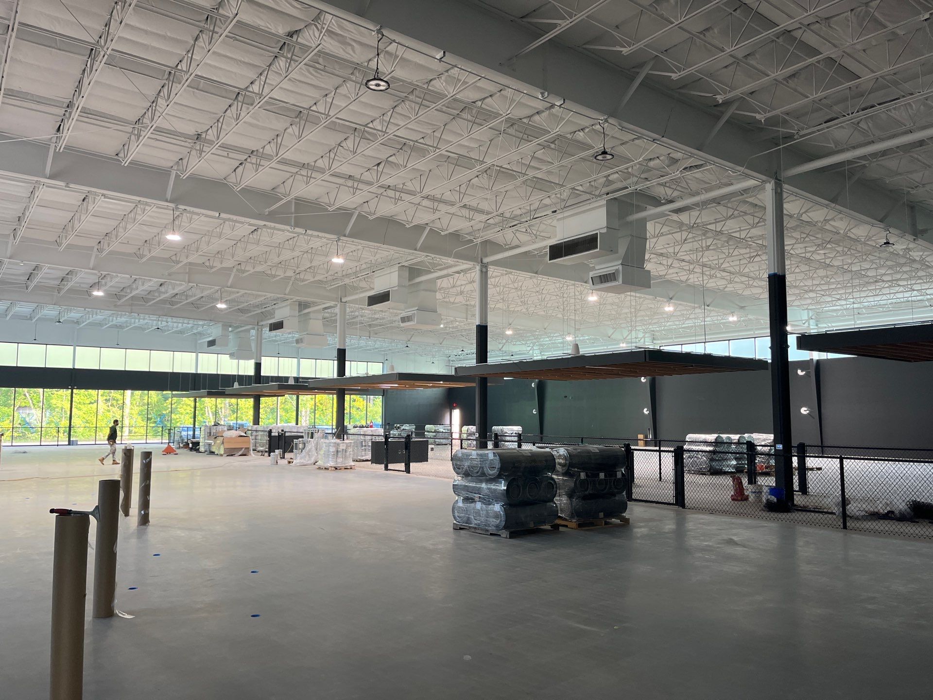Interior of a large, unfinished warehouse or commercial space with high ceilings, stacked materials, and construction equipment.
