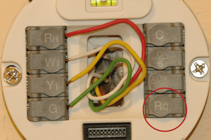 Close-up of a thermostat wiring panel showing multiple colored wires connected to labeled terminals; the "RC" terminal is highlighted with a red circle.