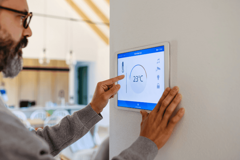 A person adjusts a smart thermostat mounted on a wall, setting the temperature to 23°C in a modern, well-lit home.