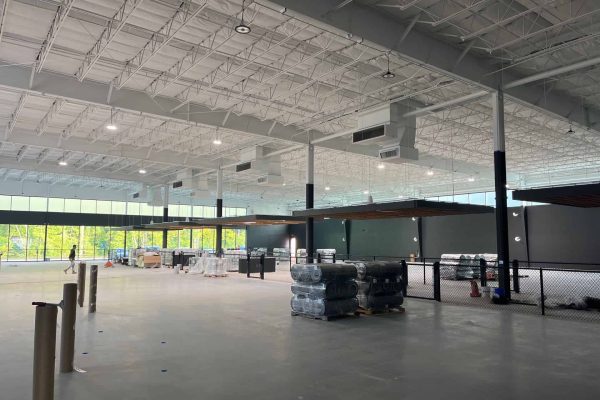 Interior of a large, unfinished warehouse or commercial space with high ceilings, stacked materials, and construction equipment.